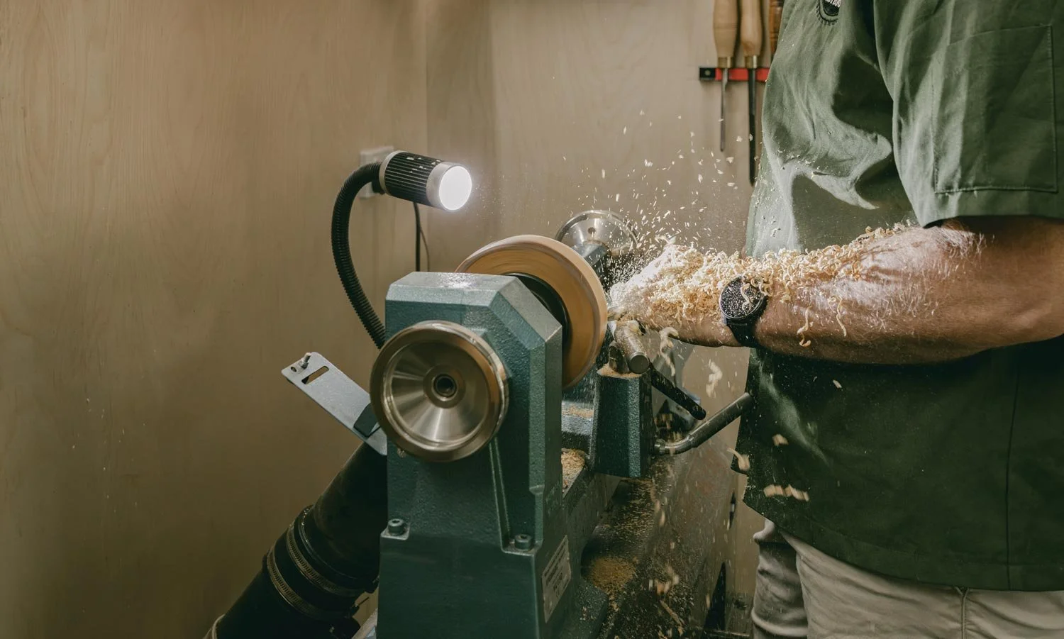 Australian wood turner, Andrew McNamara, operating a wood lathe machine, shaping a piece of wood with wood shavings flying around.