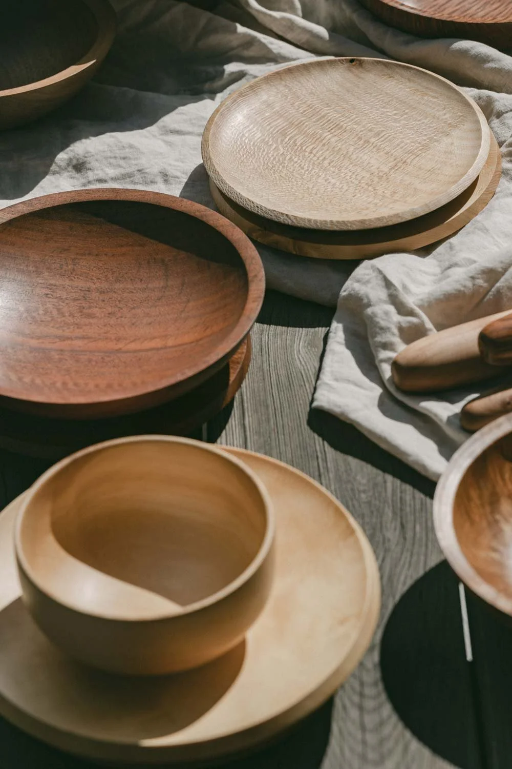 Various wooden bowls and plates arranged on a textured wooden surface with a light-coloured cloth underneath.