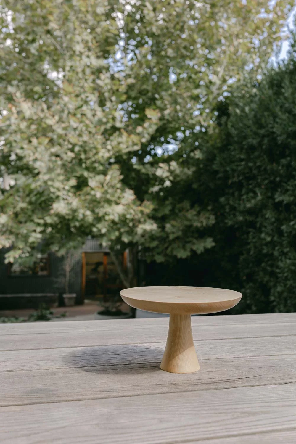 A timber cake stand placed on timber decking, with trees and a backyard in the background.