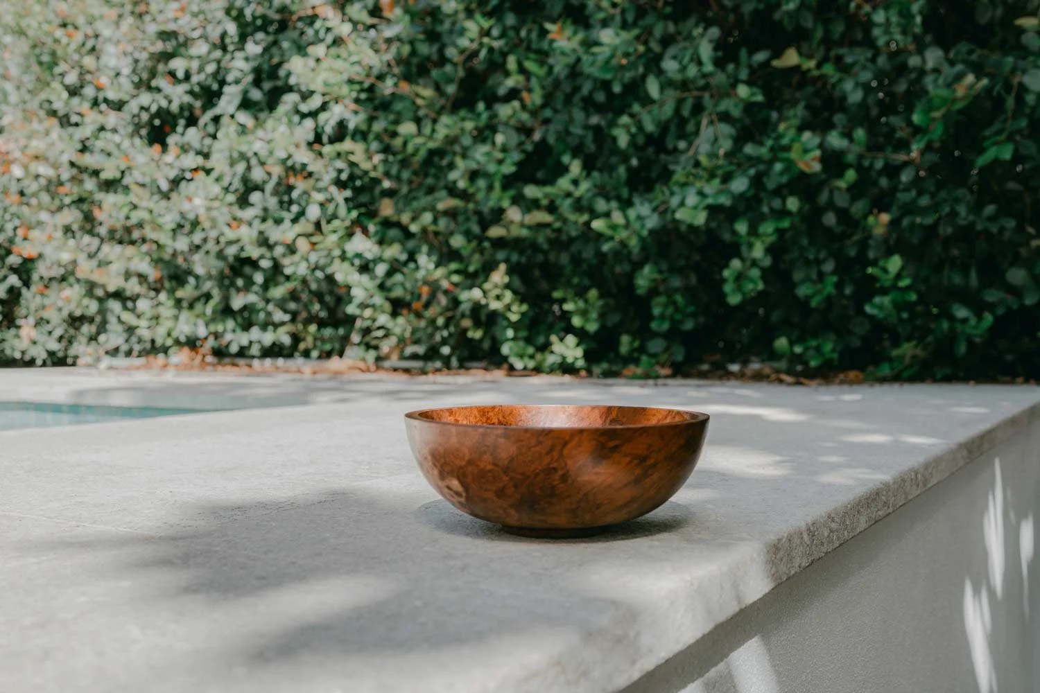 Red Mallee Burl timber bowl placed on a concrete surface with greenery in background.