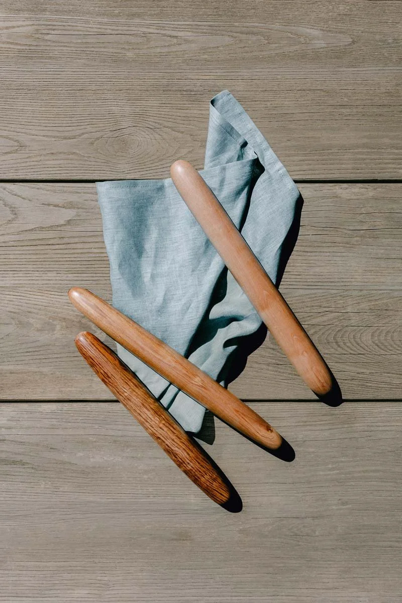 A blue cloth napkin or towel on a wooden surface with two timber rolling pins resting on top.