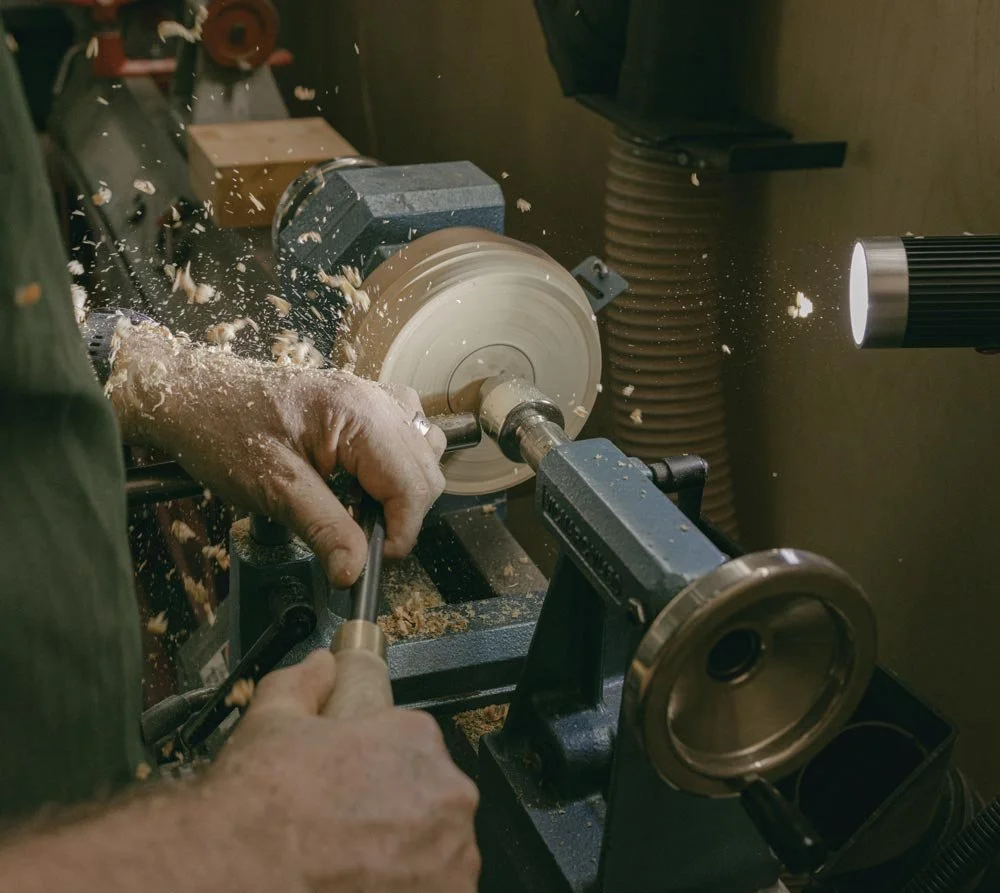 Andrew McNamara, Perth wood turner, using a lathe to shape a piece of wood, with wood shavings flying around in a woodworking workshop.