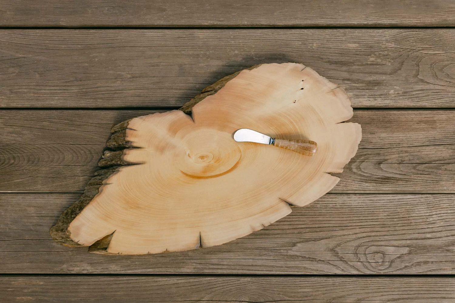 Timber platter / cutting board with a small wood-handled pate knife resting on it, placed on a wooden surface.