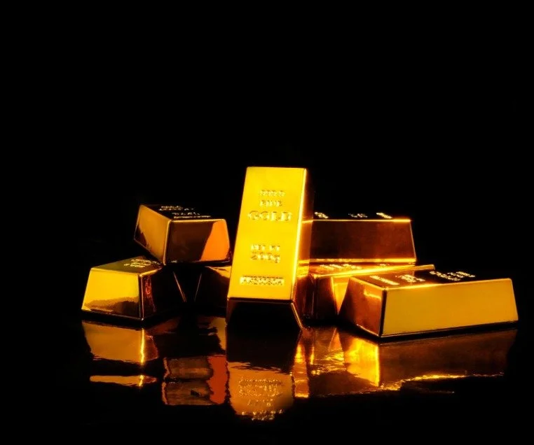 Gold bars stacked on a reflective surface against a black background.