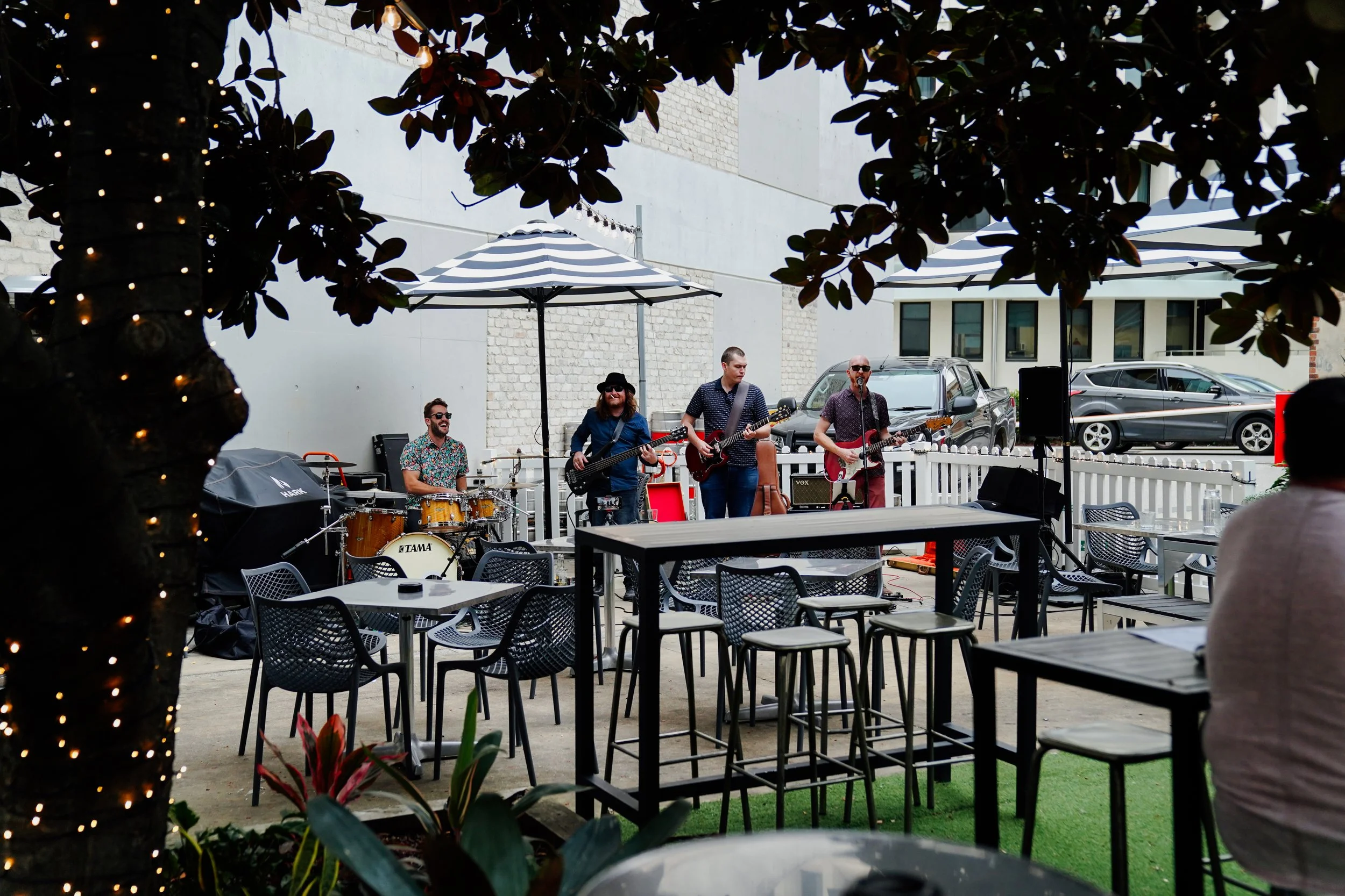 Band performing live music outdoors under umbrellas at a patio or courtyard.