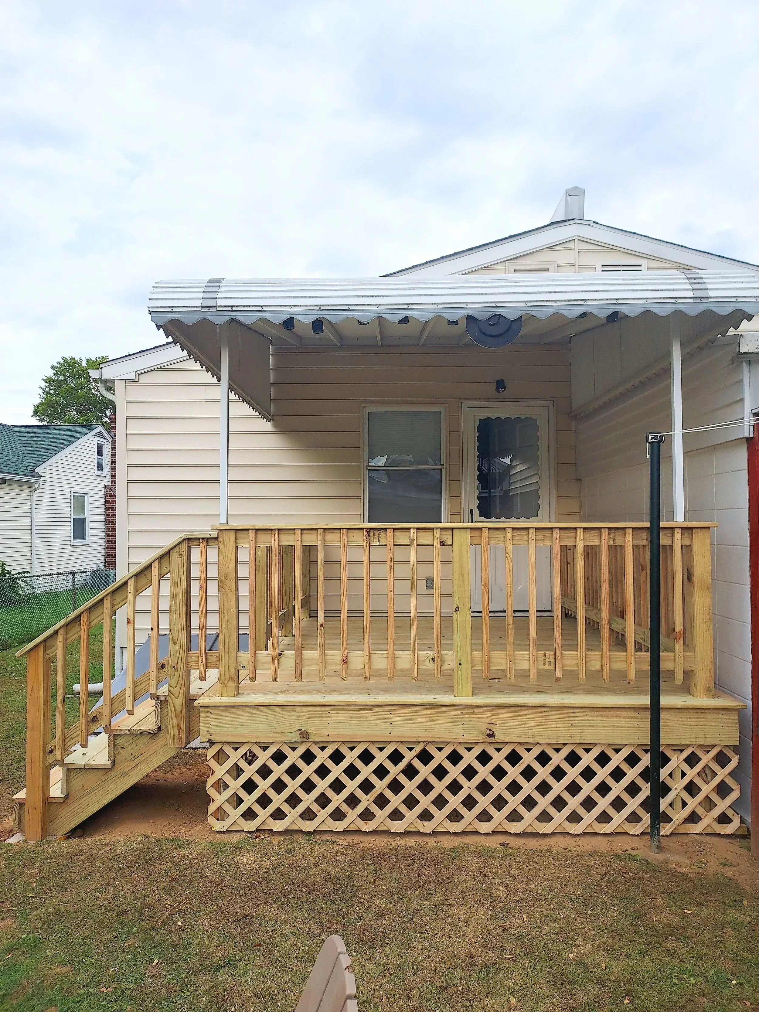 Back porch with new wooden deck, railing, stairs, and lattice under decking, attached to a beige house with vinyl siding.