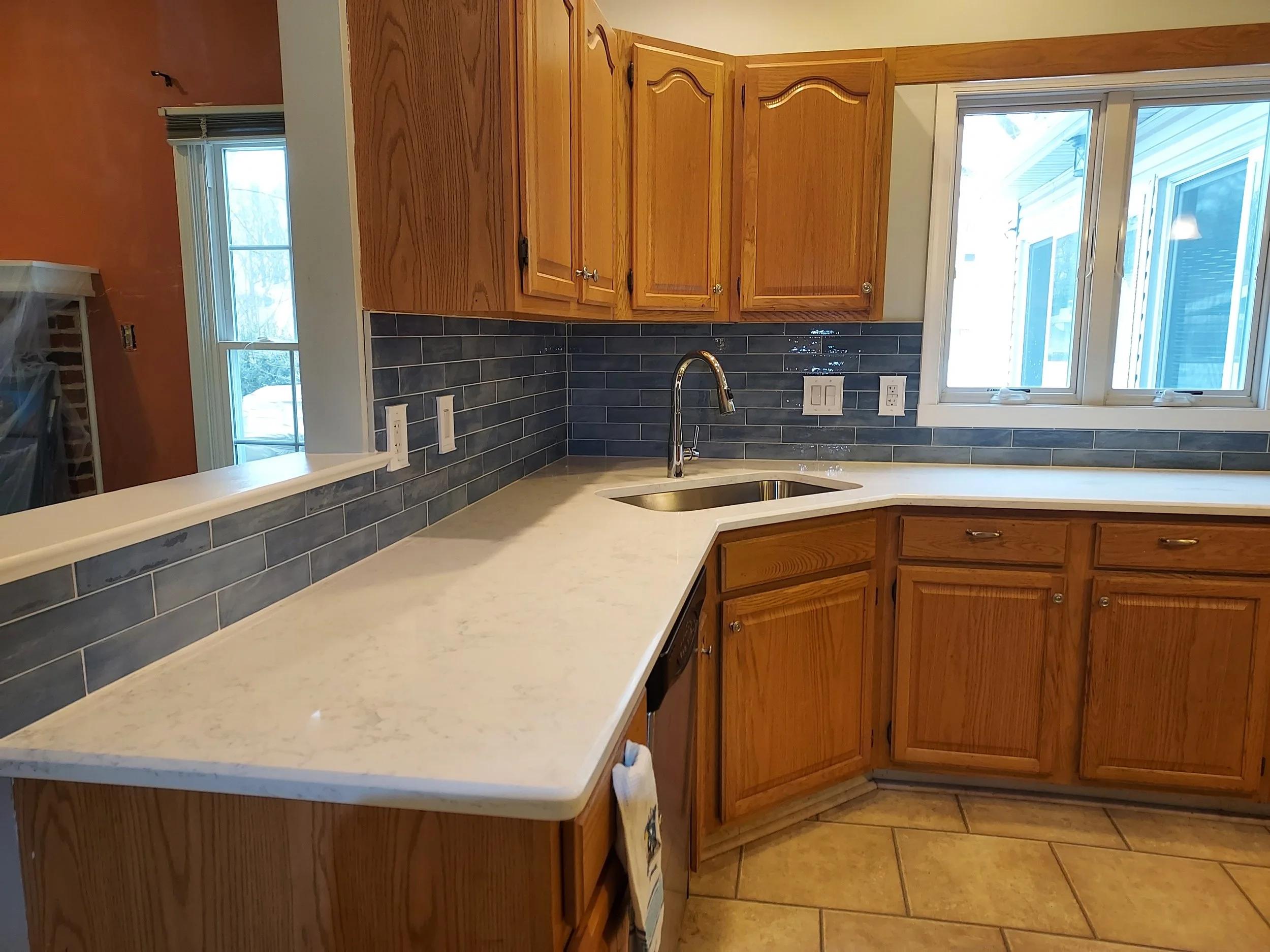 A kitchen with wooden cabinets, a marble countertop, a stainless steel sink, and a blue tile backsplash.