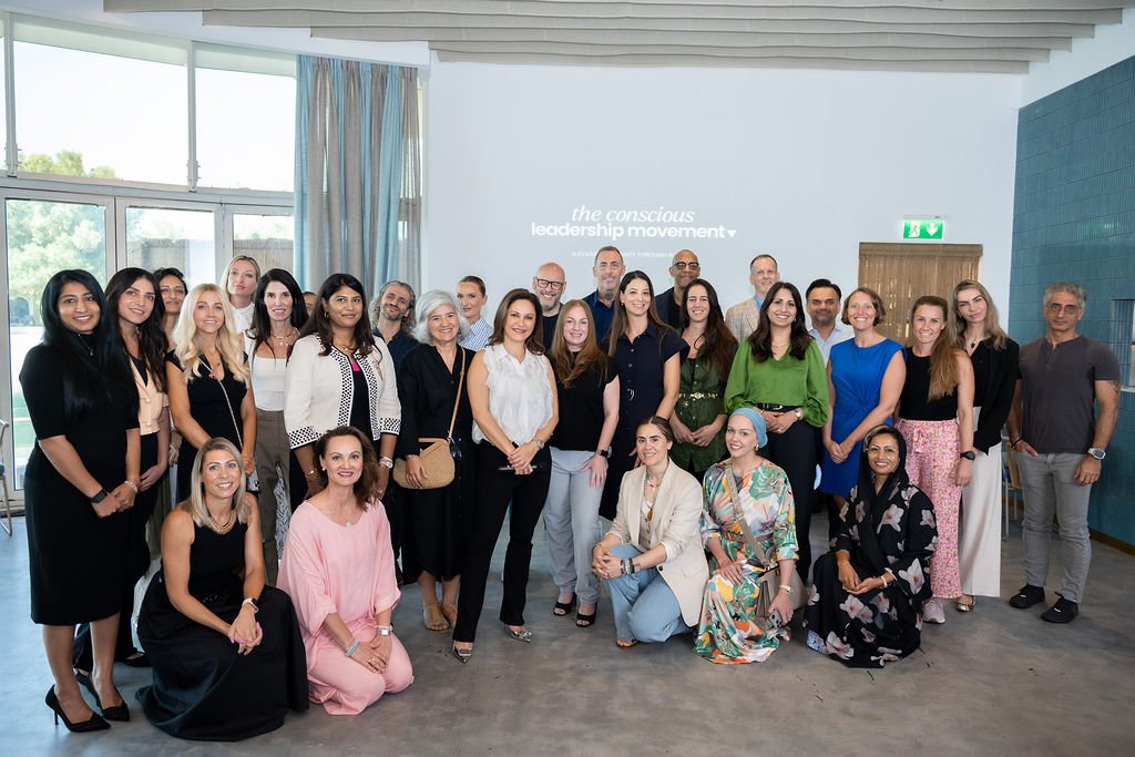 Group of diverse professionals posing indoors for a photo, with a projection on the wall reading 'the conscious leadership movement'.