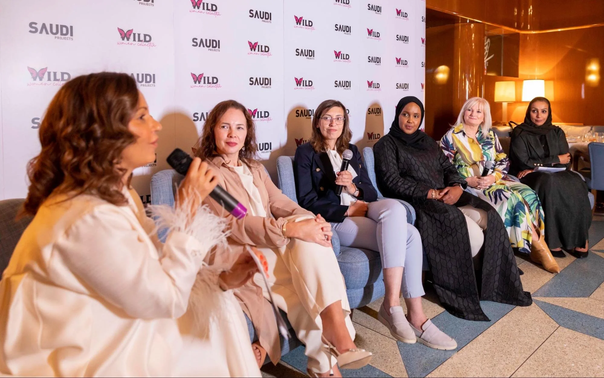 A group of women sitting in a row at a panel discussion, with a backdrop displaying logos of Saudi Projects and WILD women collective.
