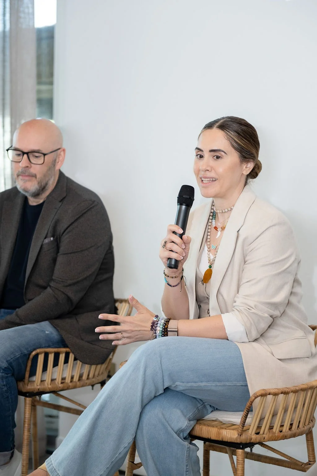 A woman holding a microphone and speaking during a panel discussion, with a man sitting next to her listening.