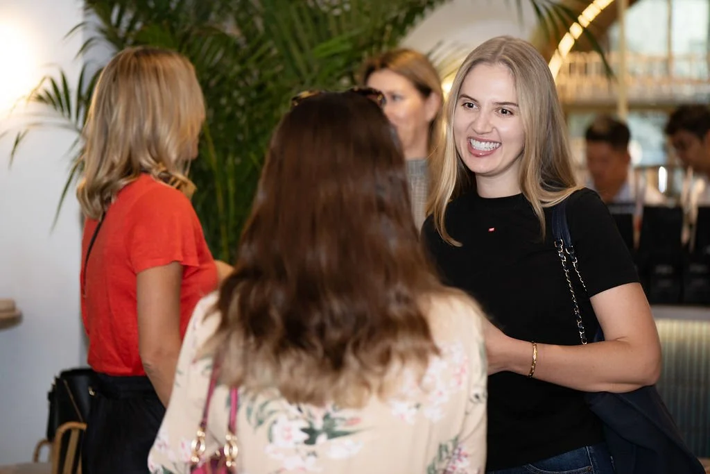 A woman smiling and engaging in conversation at a social gathering, with others in the background.
