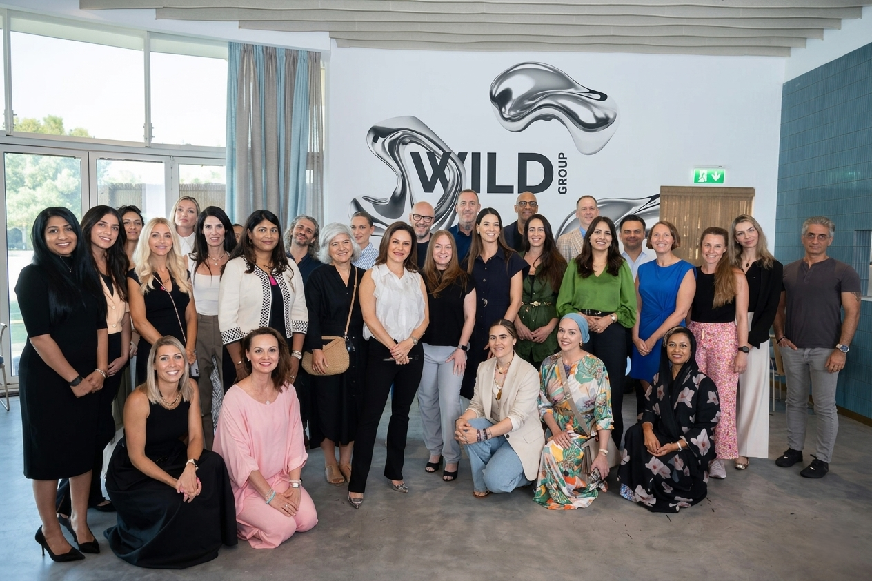 Group of diverse professionals posing indoors, with a modern logo that says 'WILD GROUP' behind them.