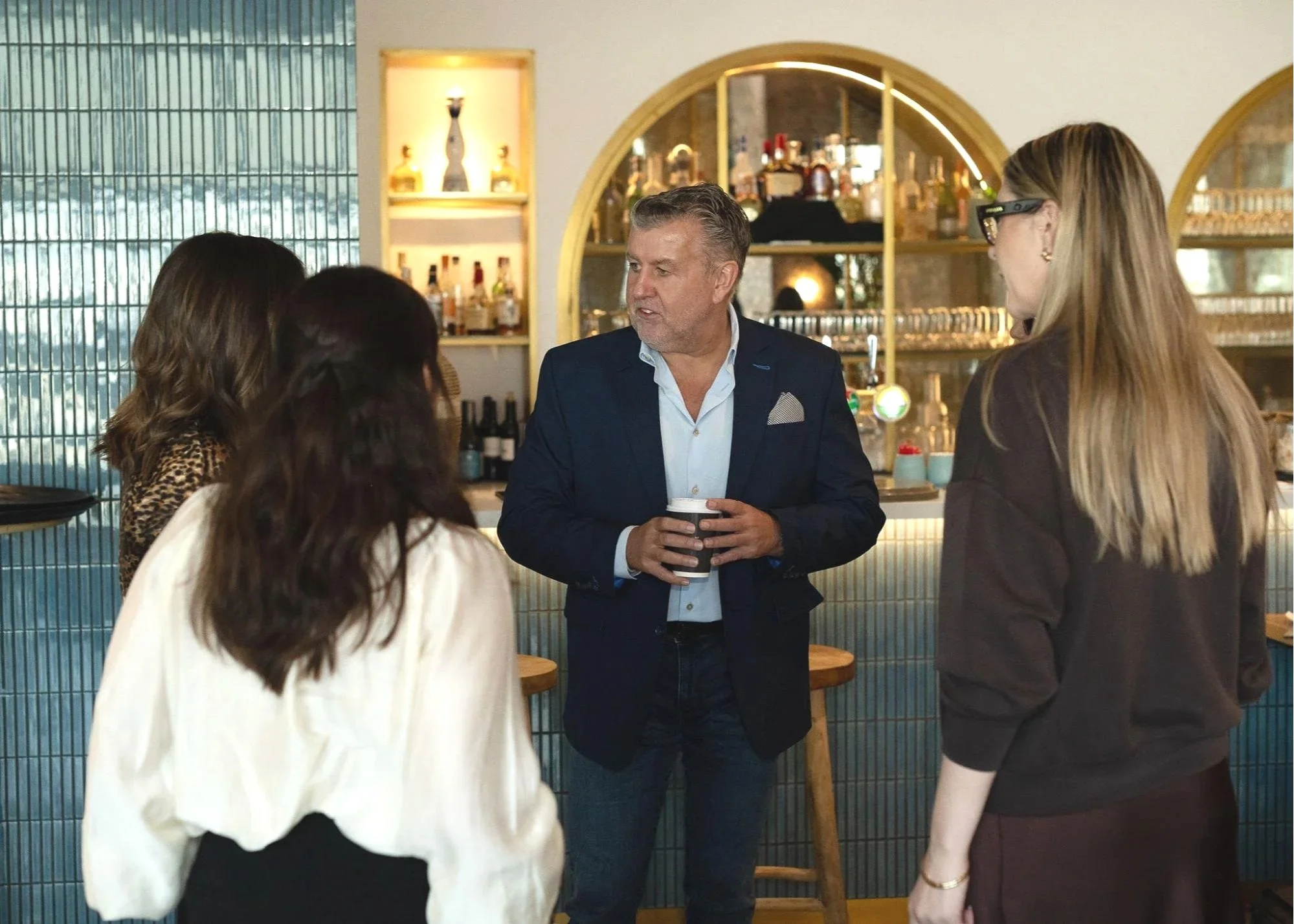 Four people having a conversation in a bar or restaurant, with a bartender or server behind the counter.