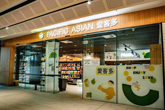 View of a Pacific Asian convenience store at an airport or shopping area, with glass doors, retail products inside, and colorful signage on the exterior.
