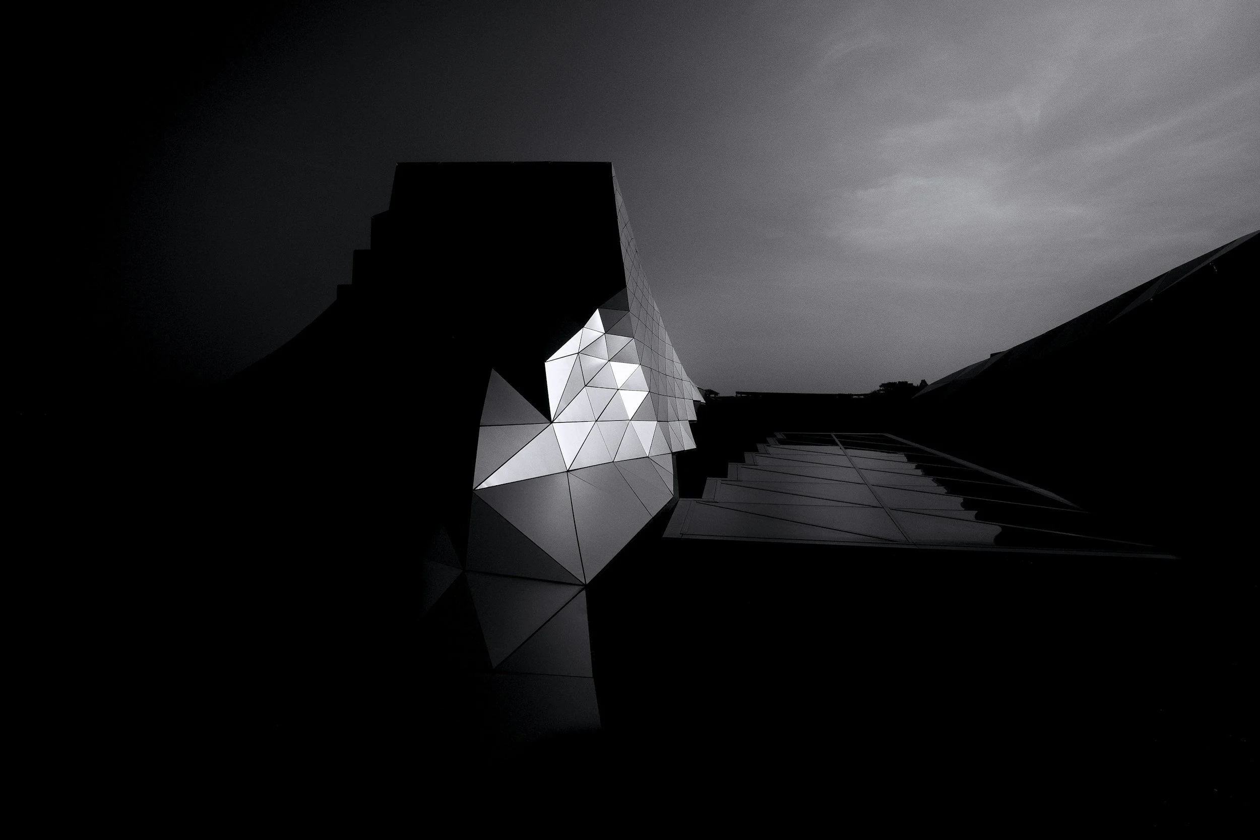 A modern building with angular, geometric design and reflective surfaces, set against a cloudy sky during daytime.