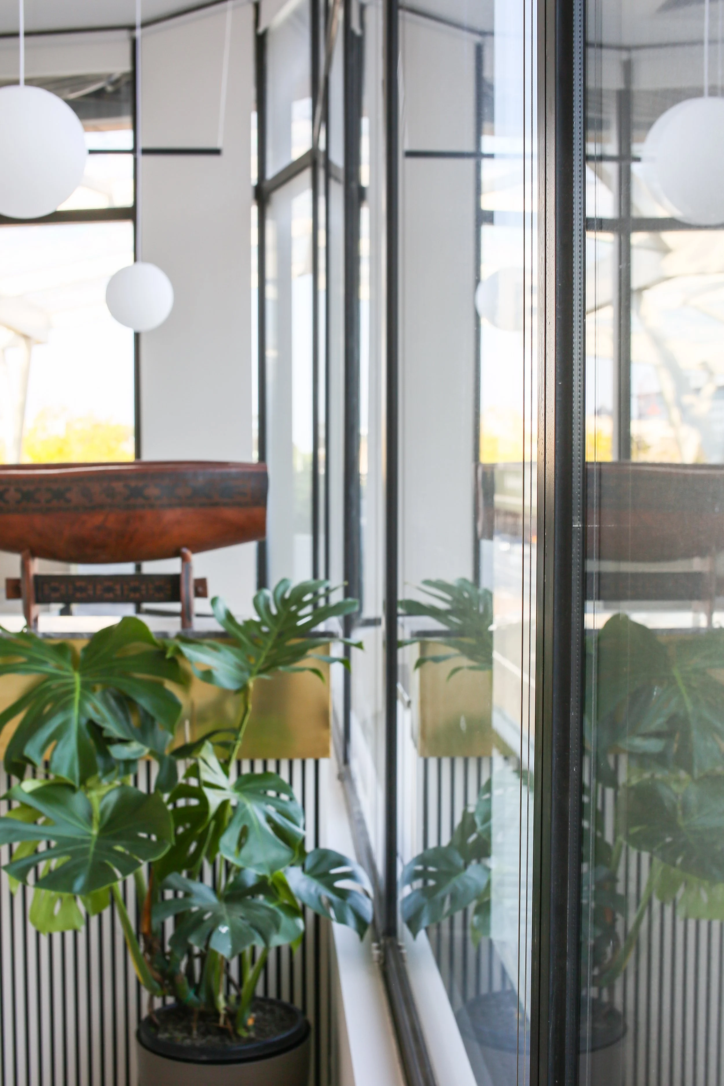 Indoor space with large glass windows, potted tropical plants, and modern spherical hanging lights.