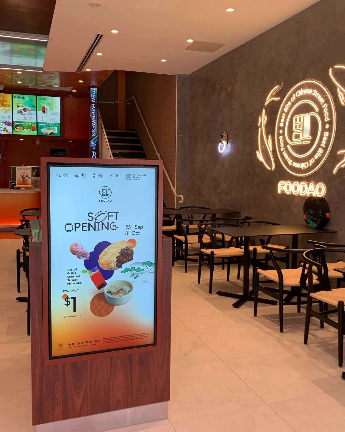 A digital menu board advertising a soft opening for a restaurant, offering selected dishes like grilled, steamed, simmered, and mooncakes for one dollar. The background interior includes dining tables and chairs, a neon sign with the restaurant's logo and name, and a staircase.
