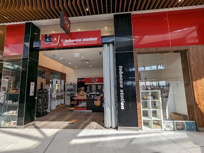 Exterior view of a tobacco store called 'Tobacco Station' with a glass storefront, display shelves inside, and a red and black sign above the entrance.