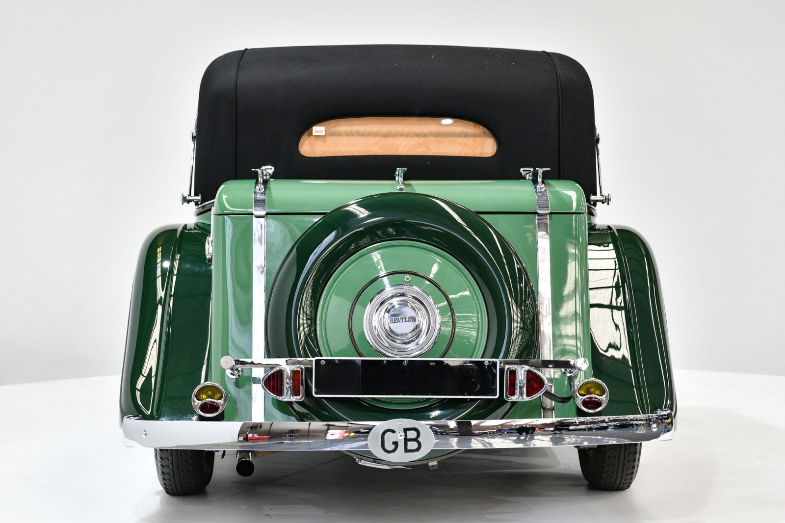Rear view of a vintage green Bentley car with a black convertible top, spare tire on the back, and a British license plate reading GB.