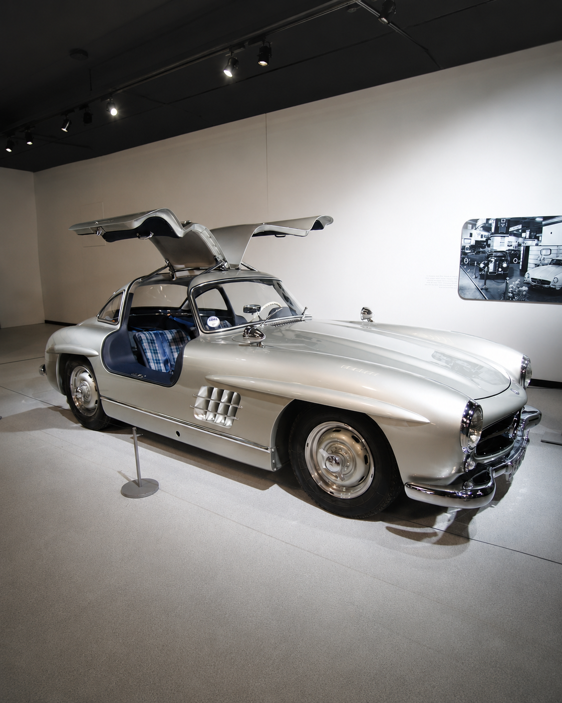 Silver vintage car with gullwing doors open on display in a museum.