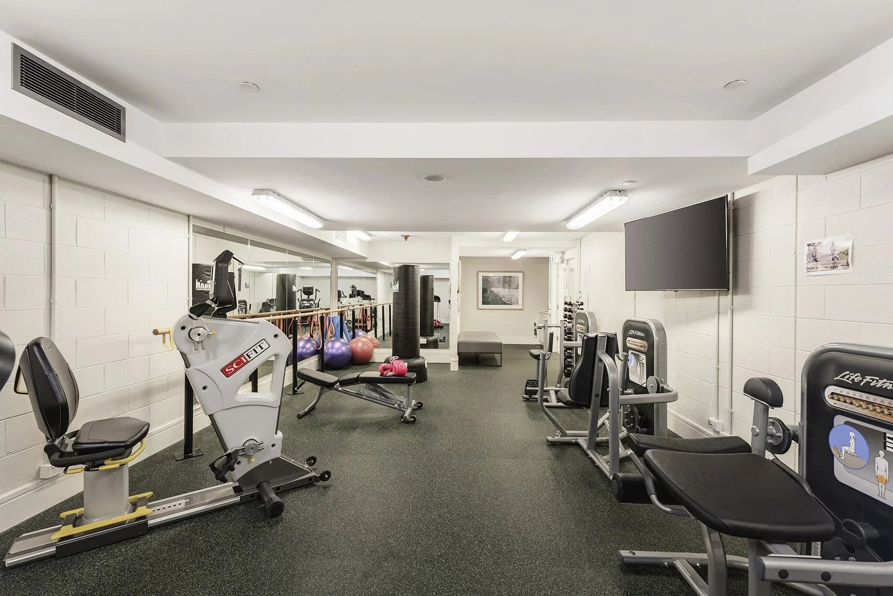A well-lit gym with exercise equipment including stationary bikes, weight machines, medicine balls, and other excercise machines and equipment, for your health and wellness.