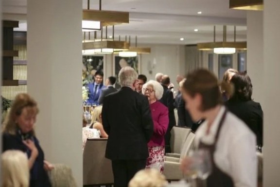People socializing at a formal event in a well-lit, elegant room.