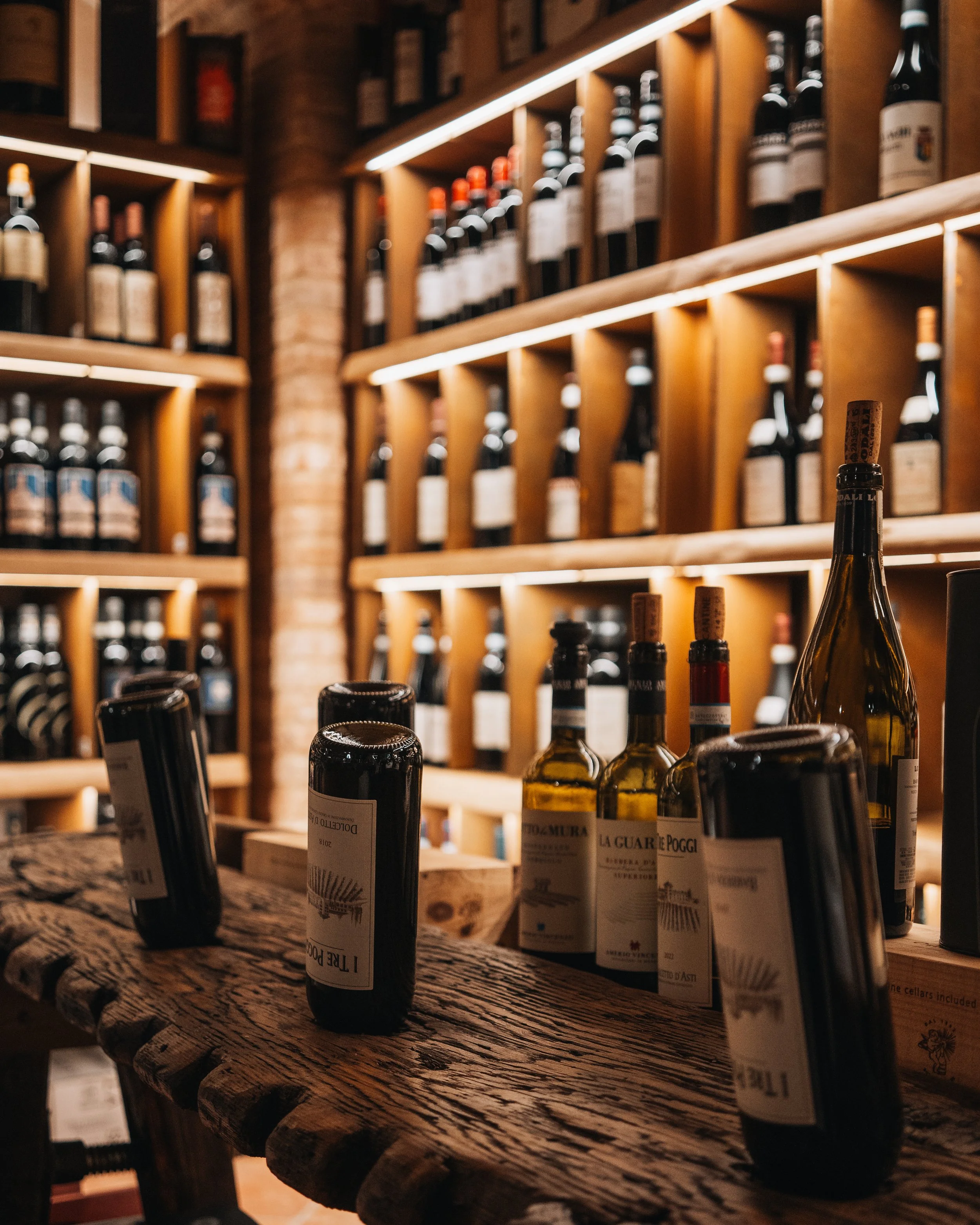 Stelle di vino su un tavolo di legno in una cantina o enoteca con scaffali di bottiglie di vino sullo sfondo.