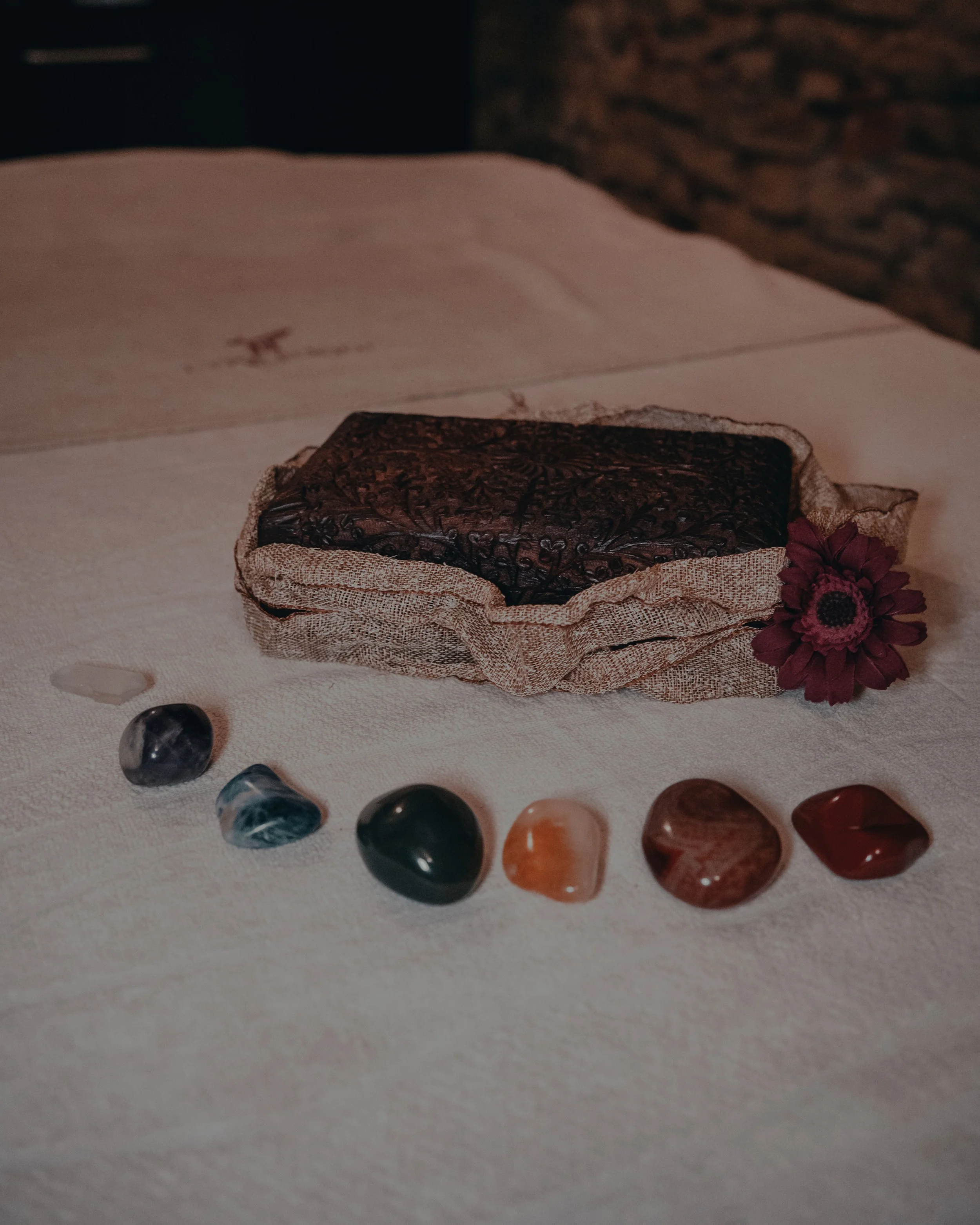 Una scatola di pietre portafortuna di vari colori e forme sul tavolo, con fiori rosso scuro a fianco.