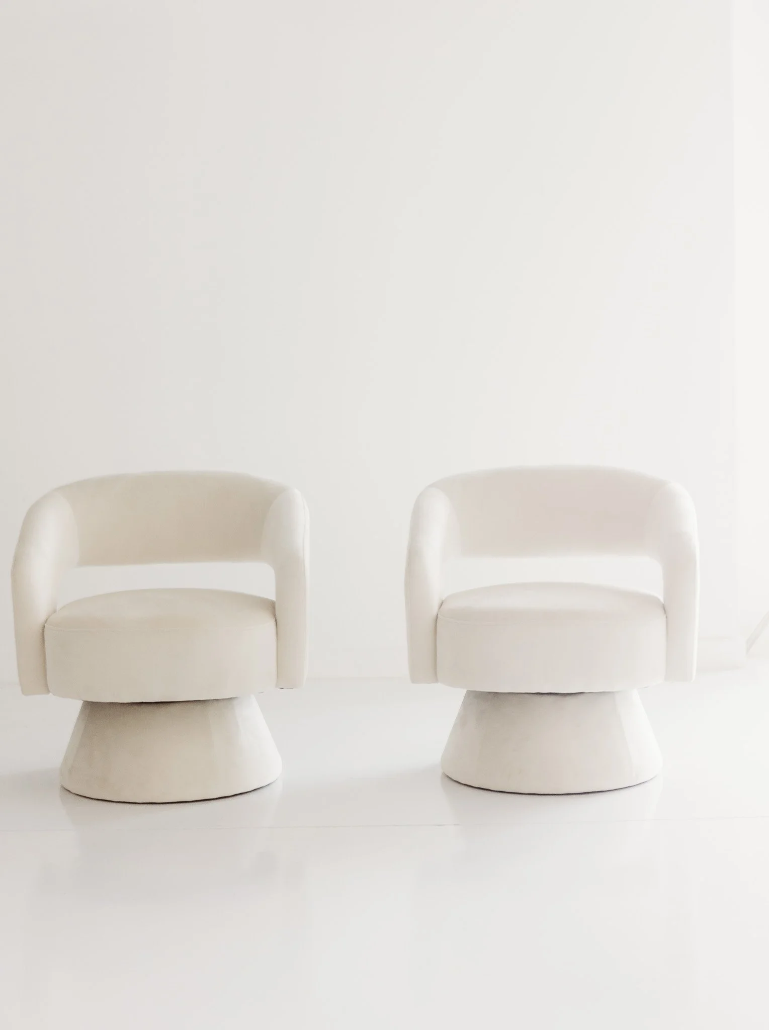 Two identical white chairs with curved armrests and high backrests placed side by side on a white surface, against a plain white background.