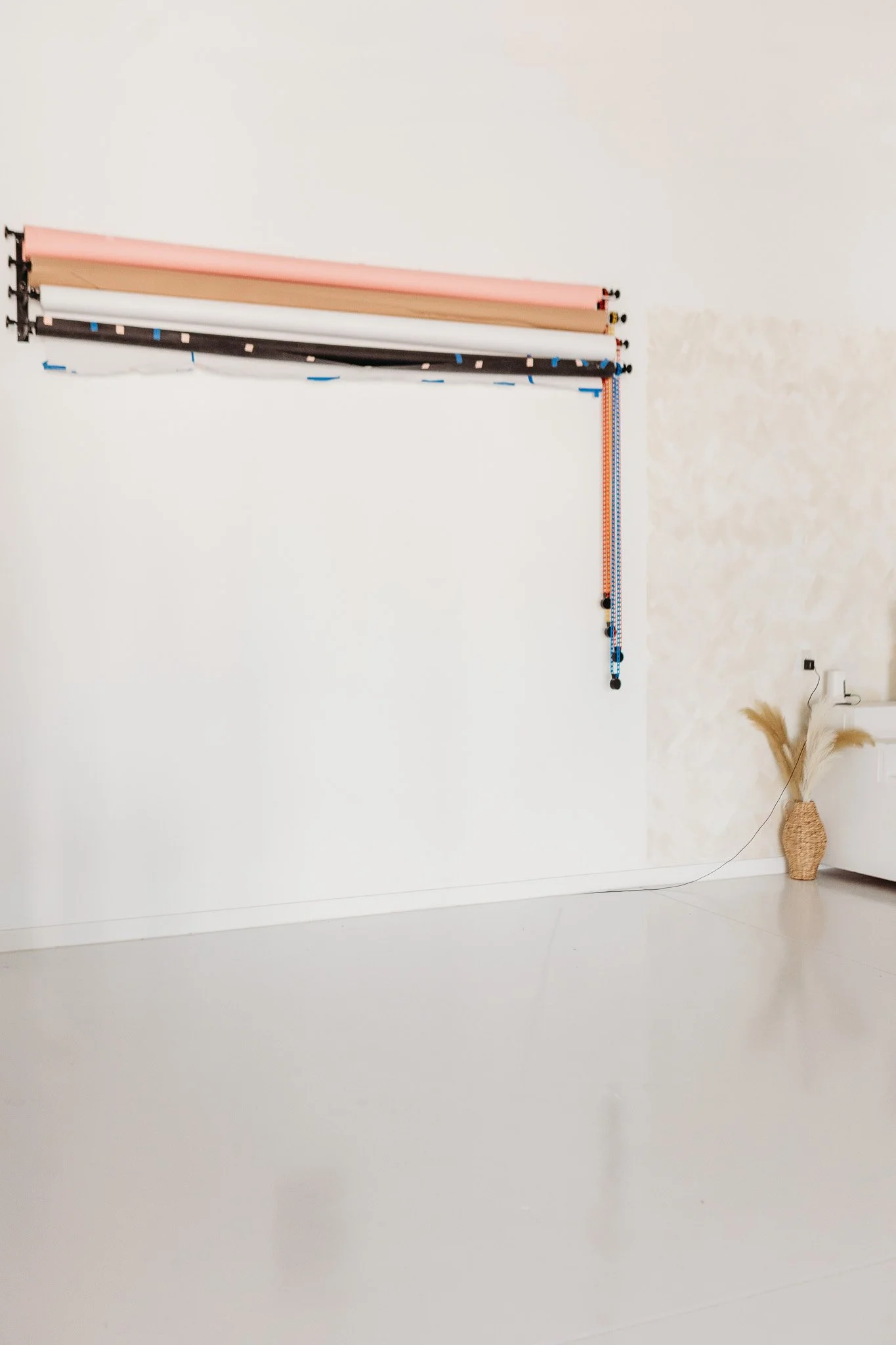 Colorful rolls of wrapping paper hung vertically on a wall, with a dry plant in a woven basket on the floor nearby.