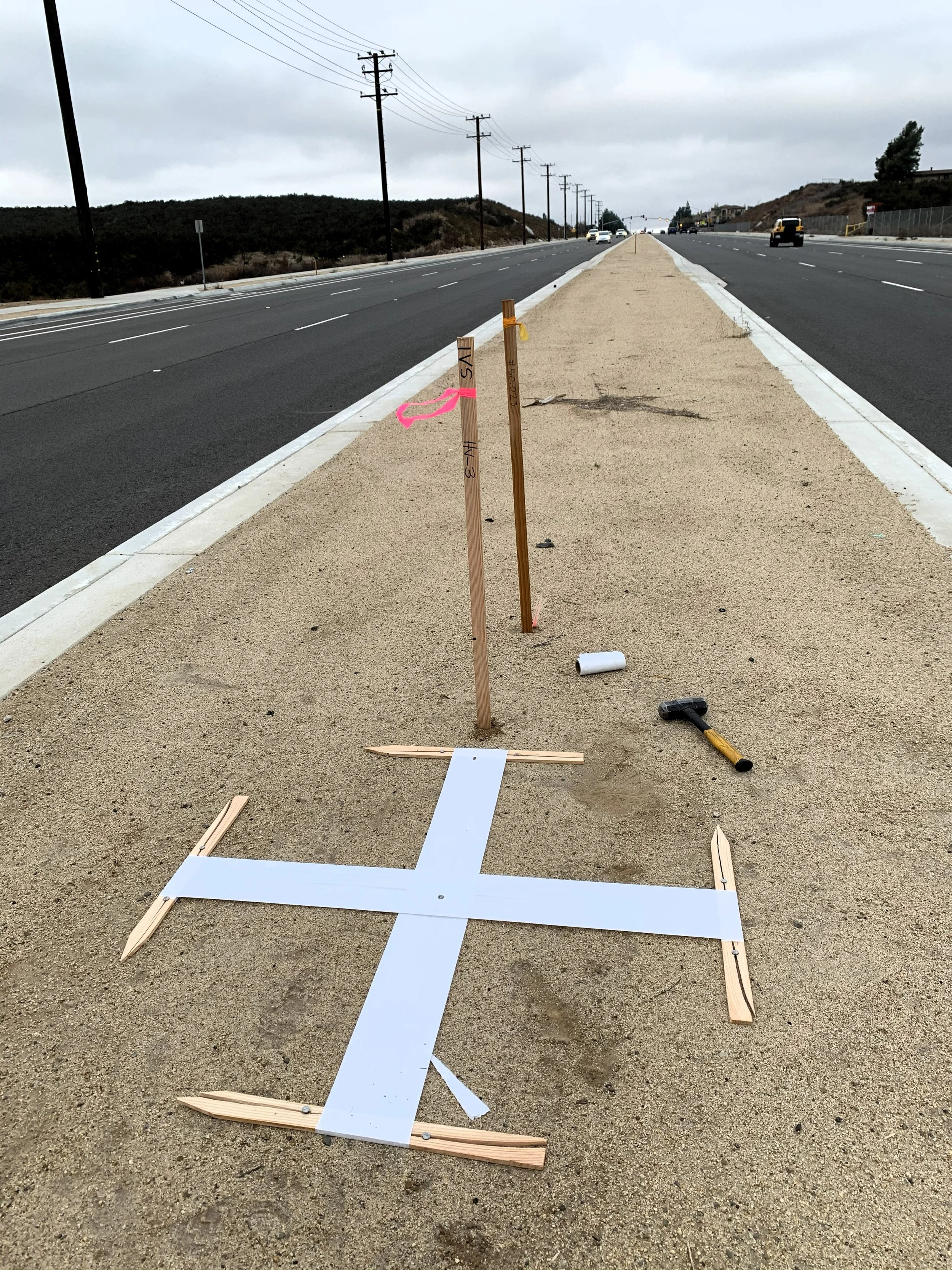 Construction site on the side of a road with a wooden frame and white panel on the ground, indicating line markings for a new road or sidewalk, with tools and stakes nearby. aerial targets for drone or plane surveying, topographic survey. aerial cont