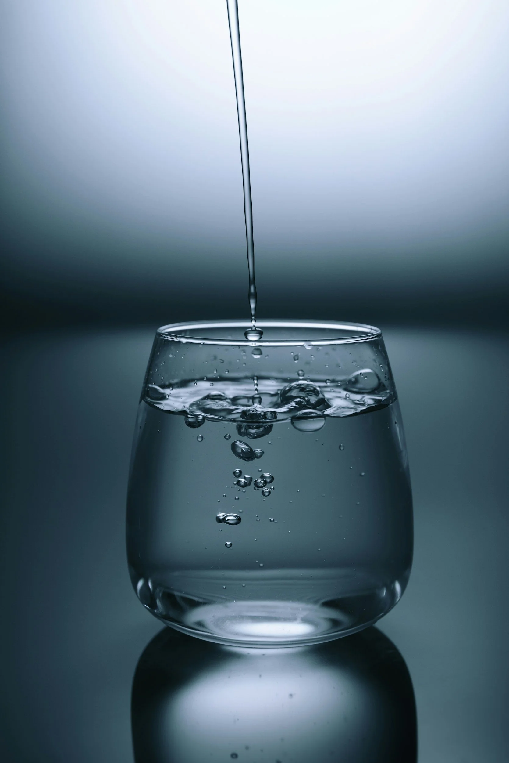 Ein Glas Wasser mit Wassertröpfchen und ein Wassertropfen, der auf das Glas fällt.
