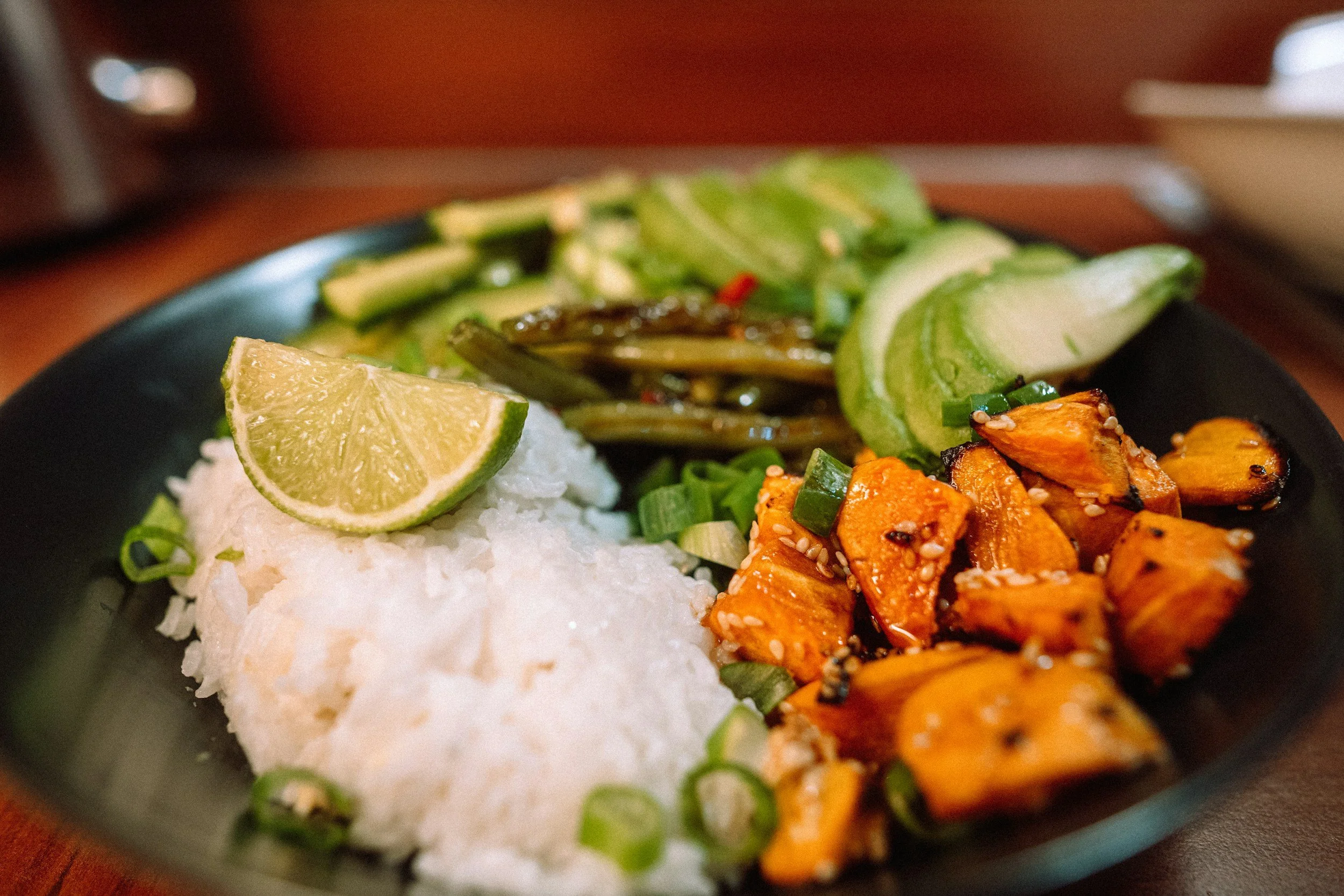 Close-up of a bowl of Japanese poke bowl with sliced cucumbers, grilled salmon, white rice, and a lime wedge.