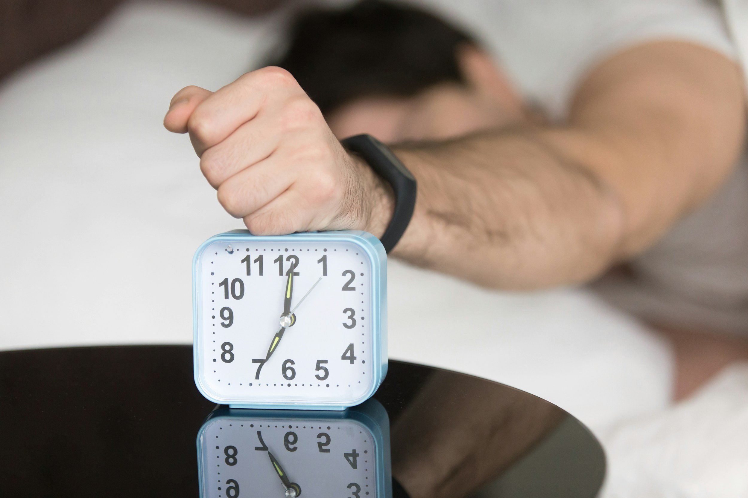 A person wearing a black watch with a white face is striking the clock's minute hand at 7, showing the time as 6:00.