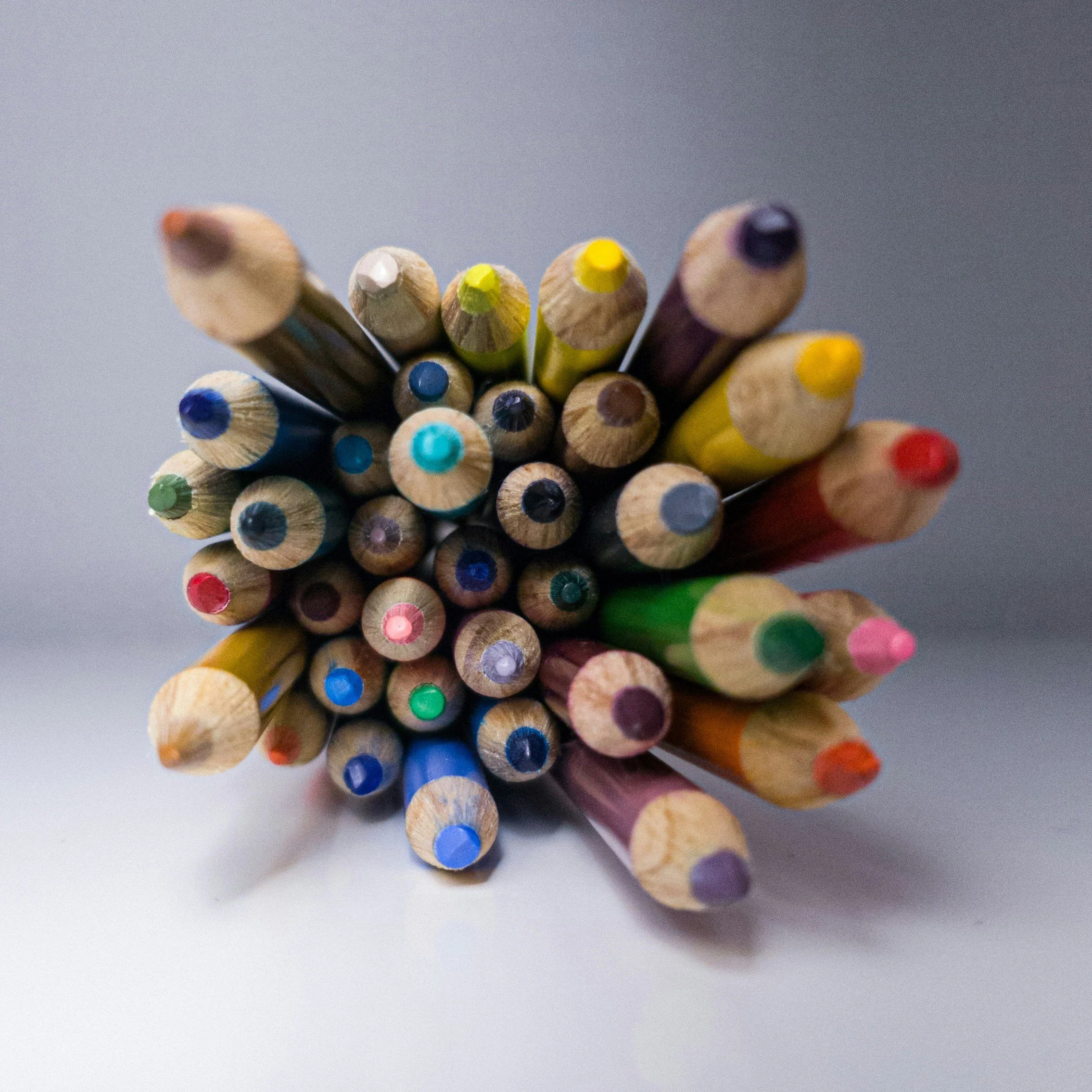 Close-up of a bundle of colored pencils arranged with tips pointing upward on a light background.