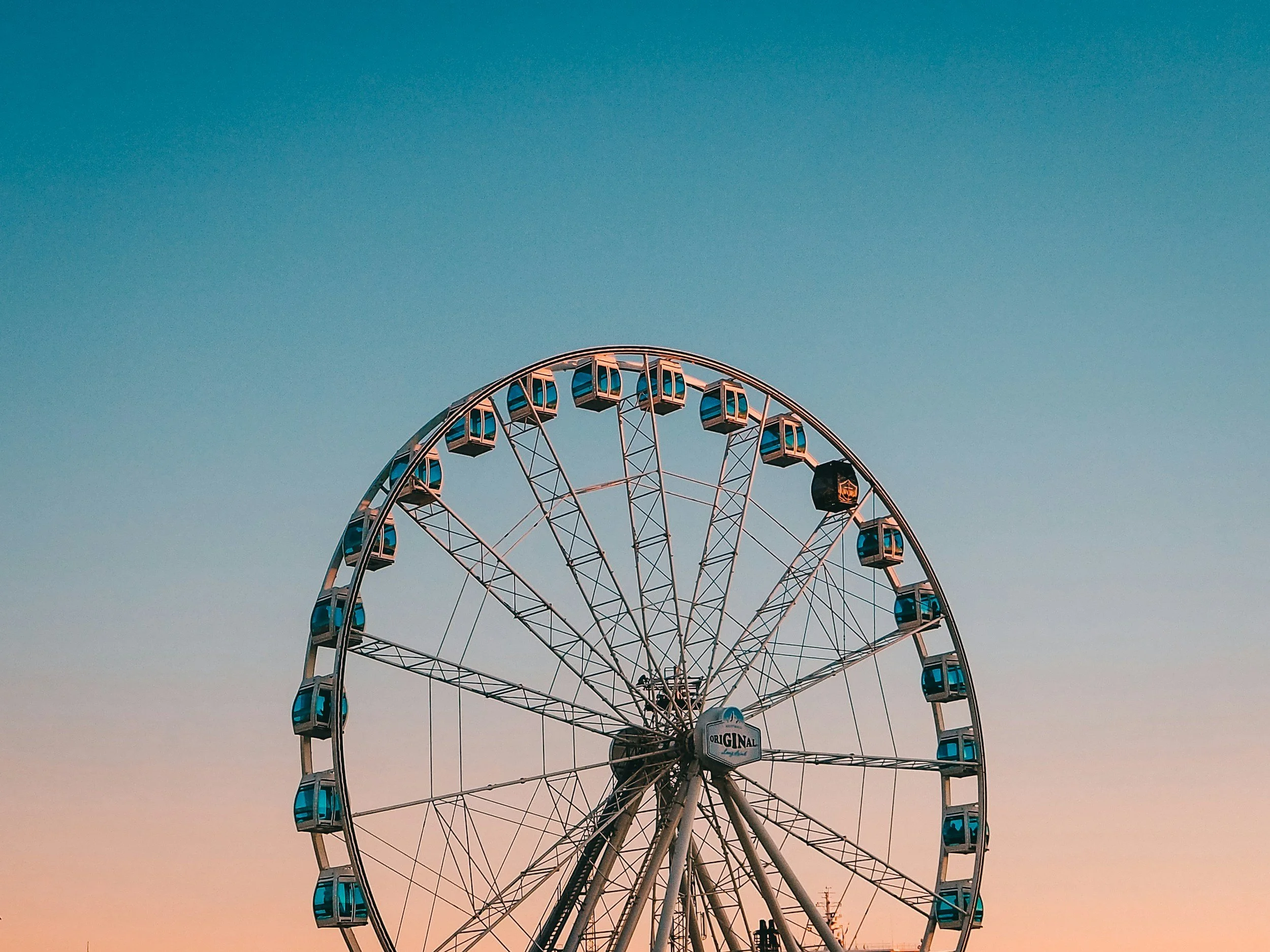 A large Ferris wheel with enclosed gondolas against a sky during sunset or sunrise.