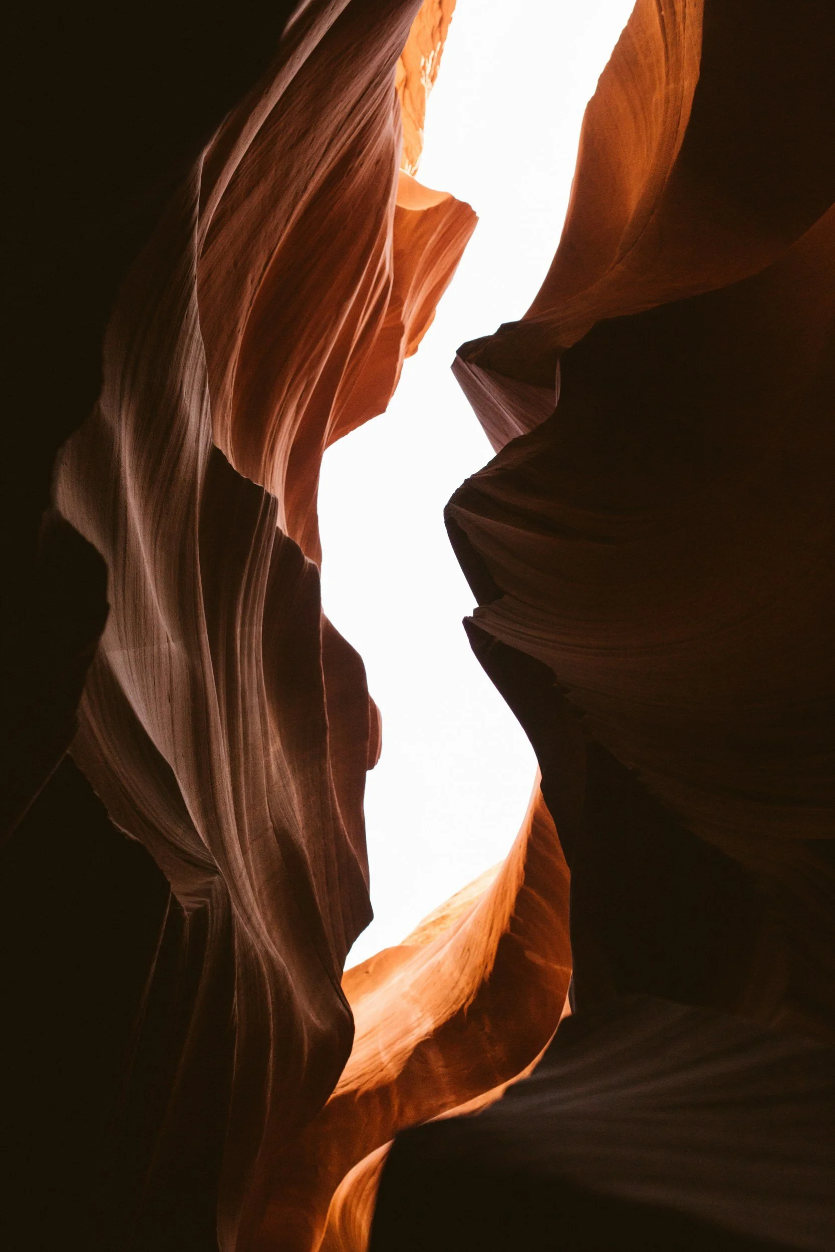 Slot canyon with smooth, flowing rock walls in shades of red, orange, and brown, with light shining from above.