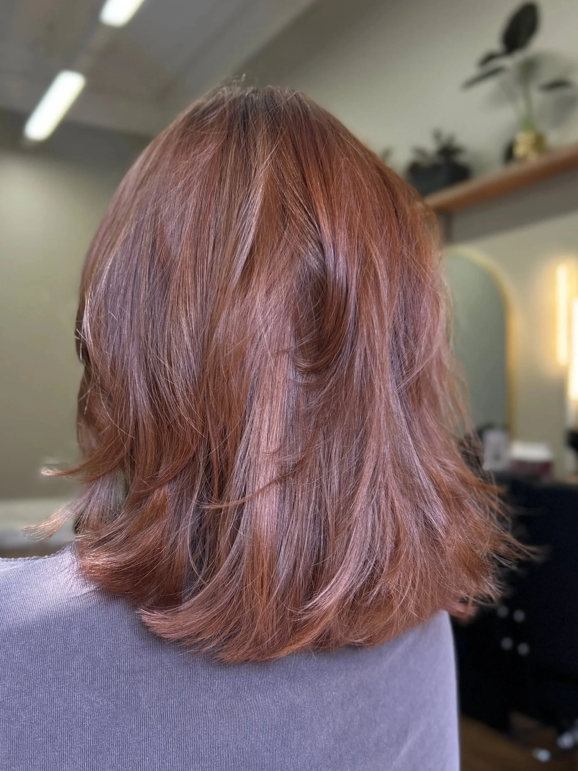 Close-up view of a woman's shoulder and hair with light pink and rose gold color, wearing a lavender or light purple top.