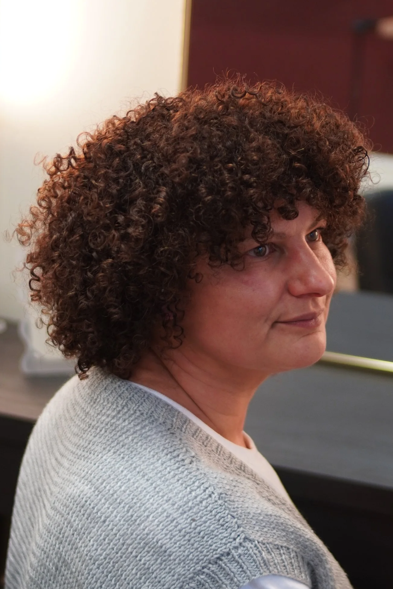 A woman with short, curly brown hair sitting in an office environment.