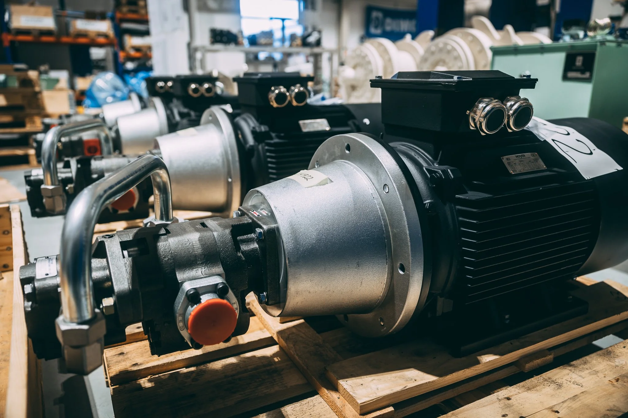 Pumpe, motor. Industrielt maskineri, motorer plassert på trestokk i et lager med hyller og utstyr i bakgrunnen.