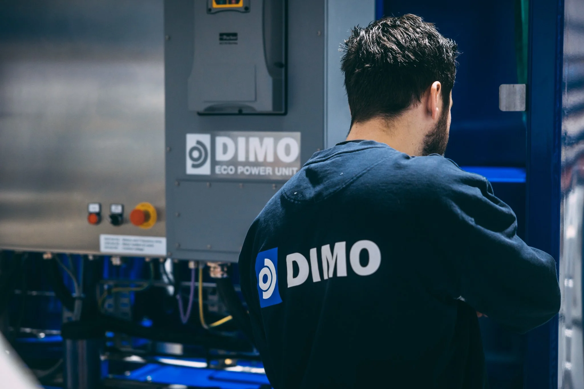 Dimo arbeider som arbeider med et elektrisk utstyr merket DIMO Eco Power Unit i et teknisk rom.