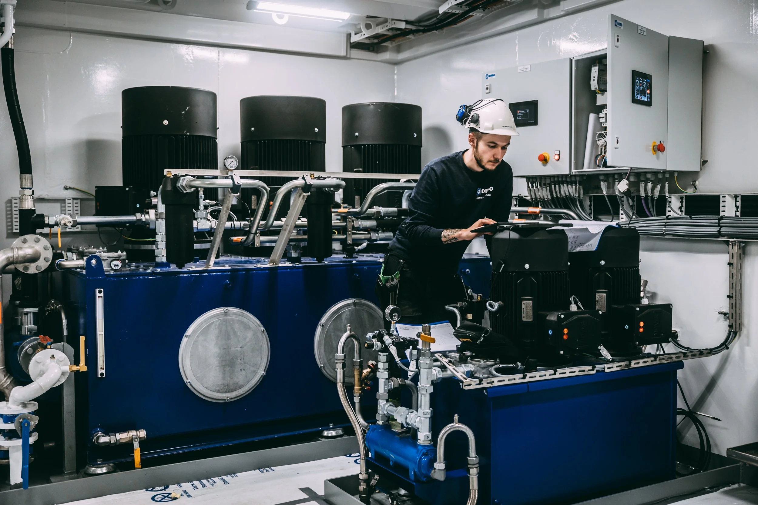 Ro Senja, EPU oppstart. Eco power unit. Berekraft, bærekraft, sustainability. Person i hjelm som arbeider med teknisk utstyr i et rom med komplekse maskiner og elektriske komponenter.