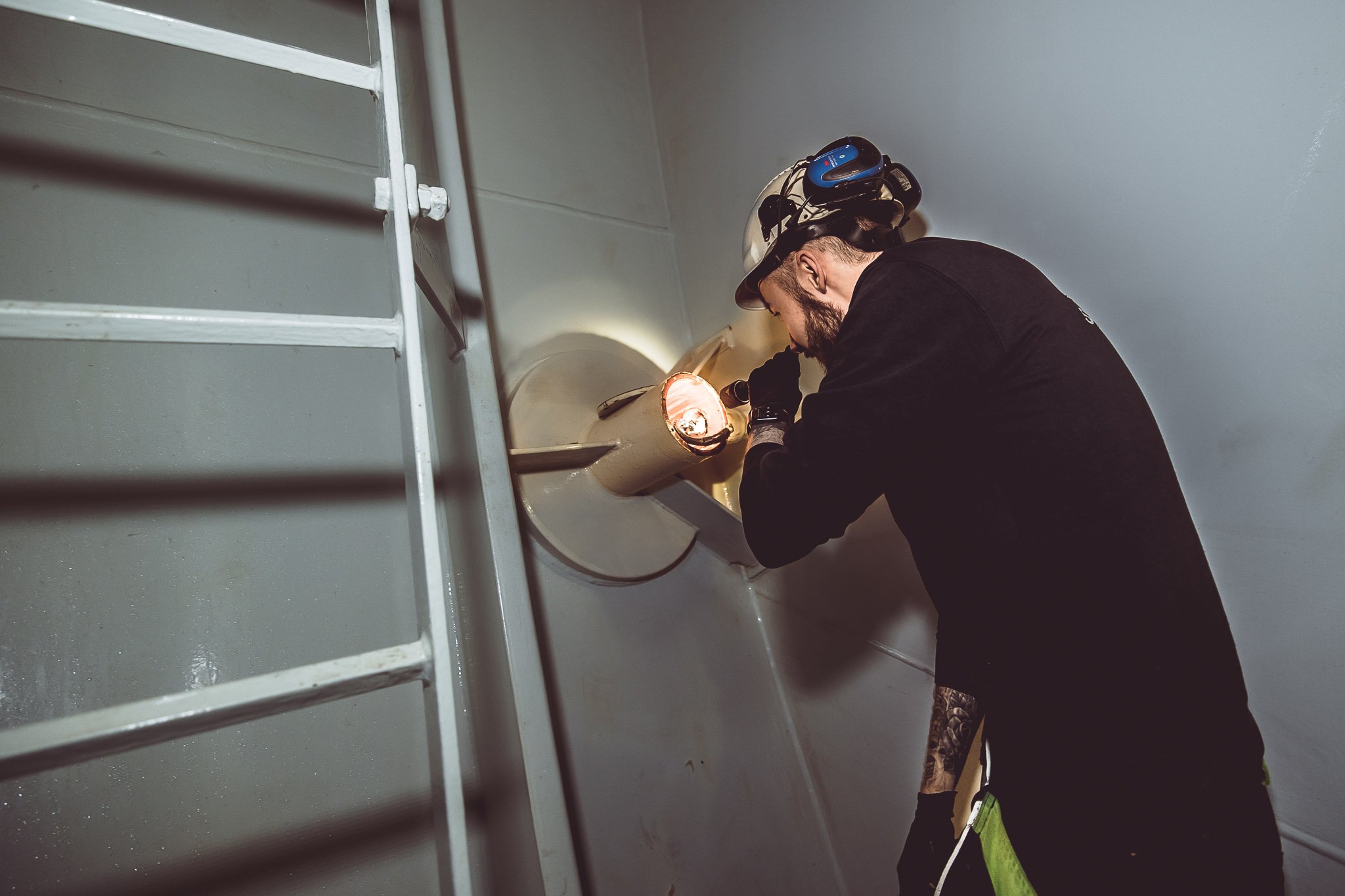 ICCP - Thomas med hjelm og verneutstyr som bruker verktøy til å jobbe på en pipe eller ventilasjon. Impressed current katodisk beskyttelse.