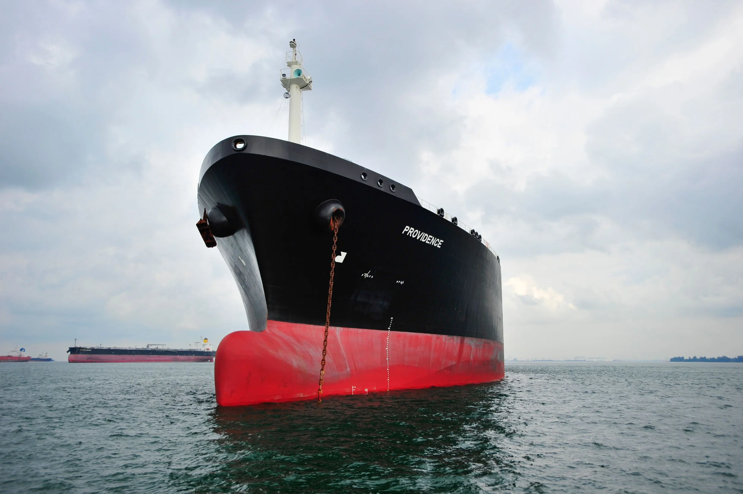 Large black and red cargo ship named Providence in the water, with other ships visible in the background under a cloudy sky.