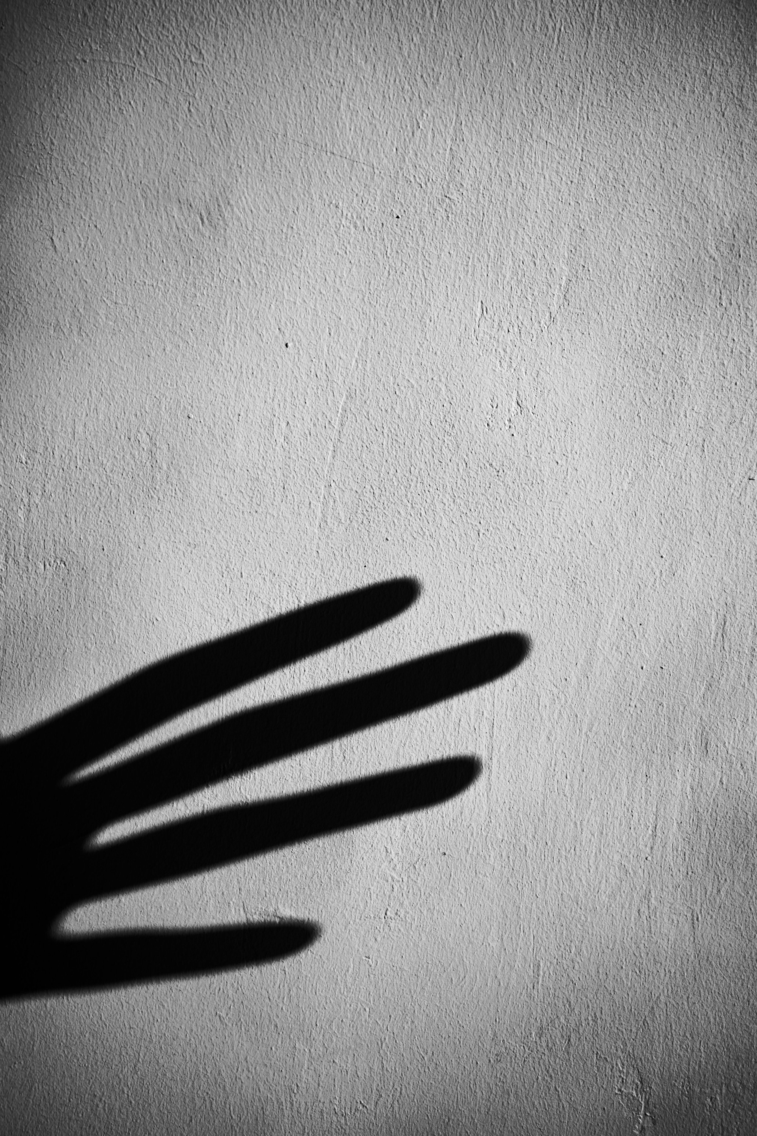A shadow of a hand on a textured white wall with shadows of fingers forming a pattern.