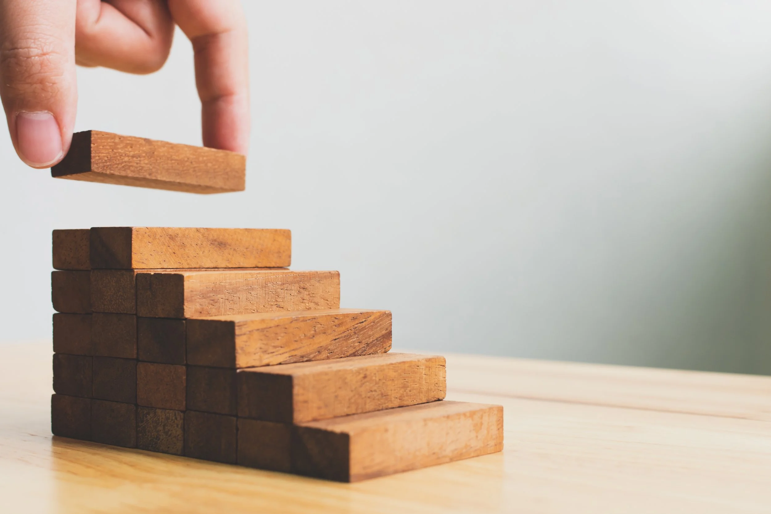 A hand is placing a wooden block on top of a stack of similar blocks, creating a tower.