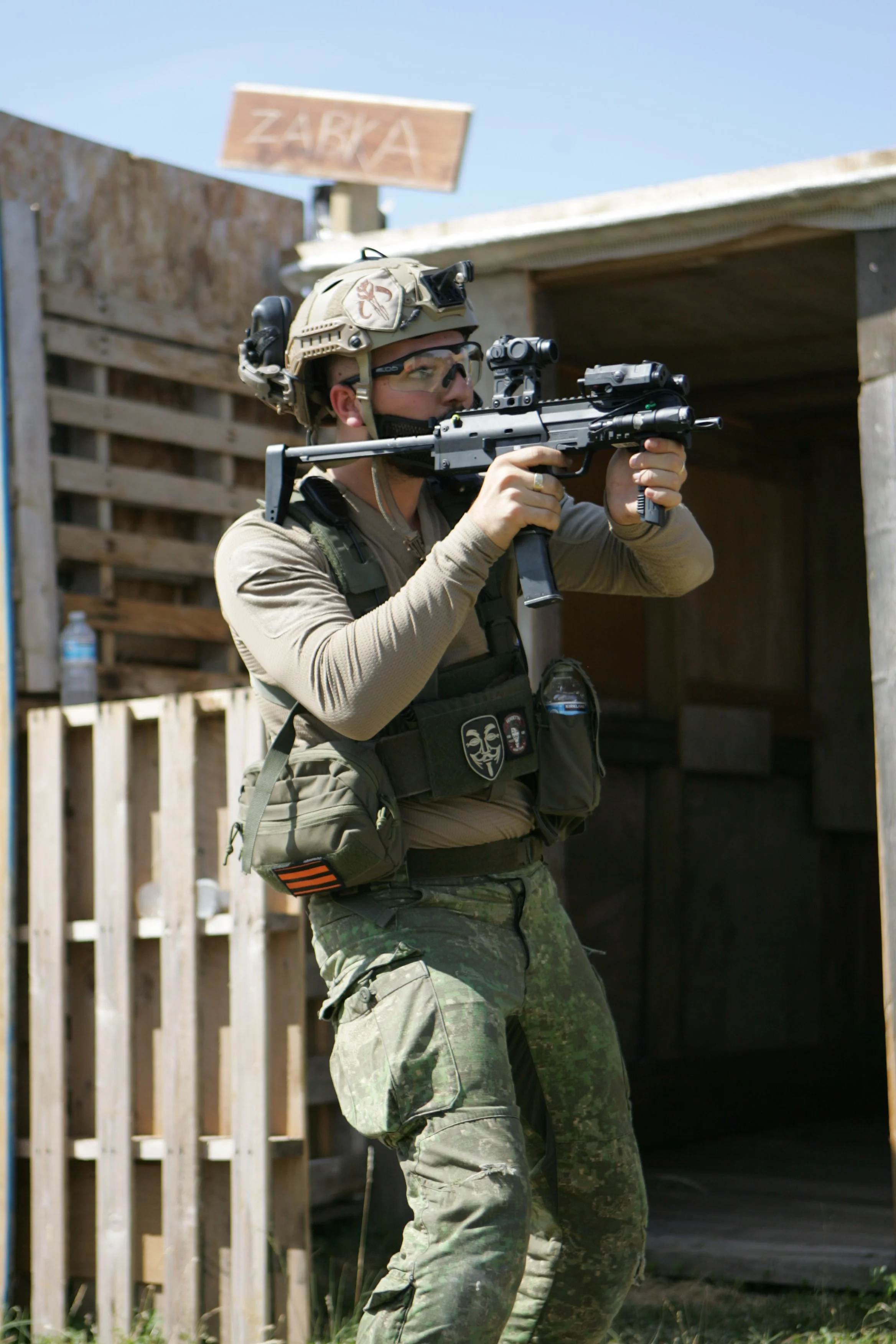 A soldier in camouflage pants aiming a rifle during training outdoors, wearing a tactical vest and helmet.