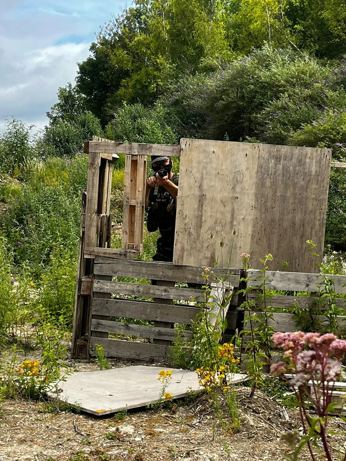 Person taking a photo of the camera in a wooden structure surrounded by greenery and flowers.