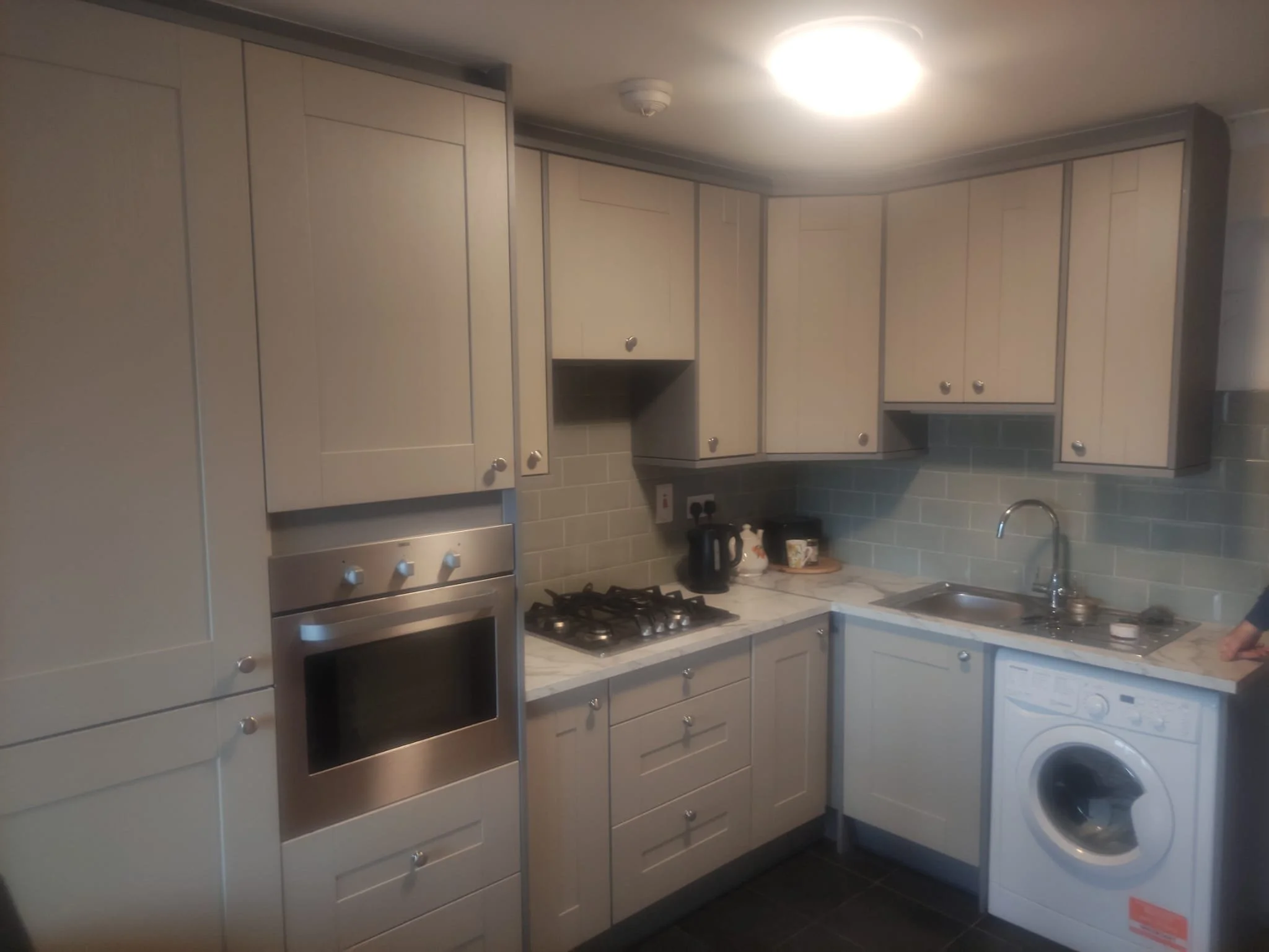 Kitchen with beige cabinets, a built-in oven, a stove, a sink, a washing machine, and a microwave on the countertop.