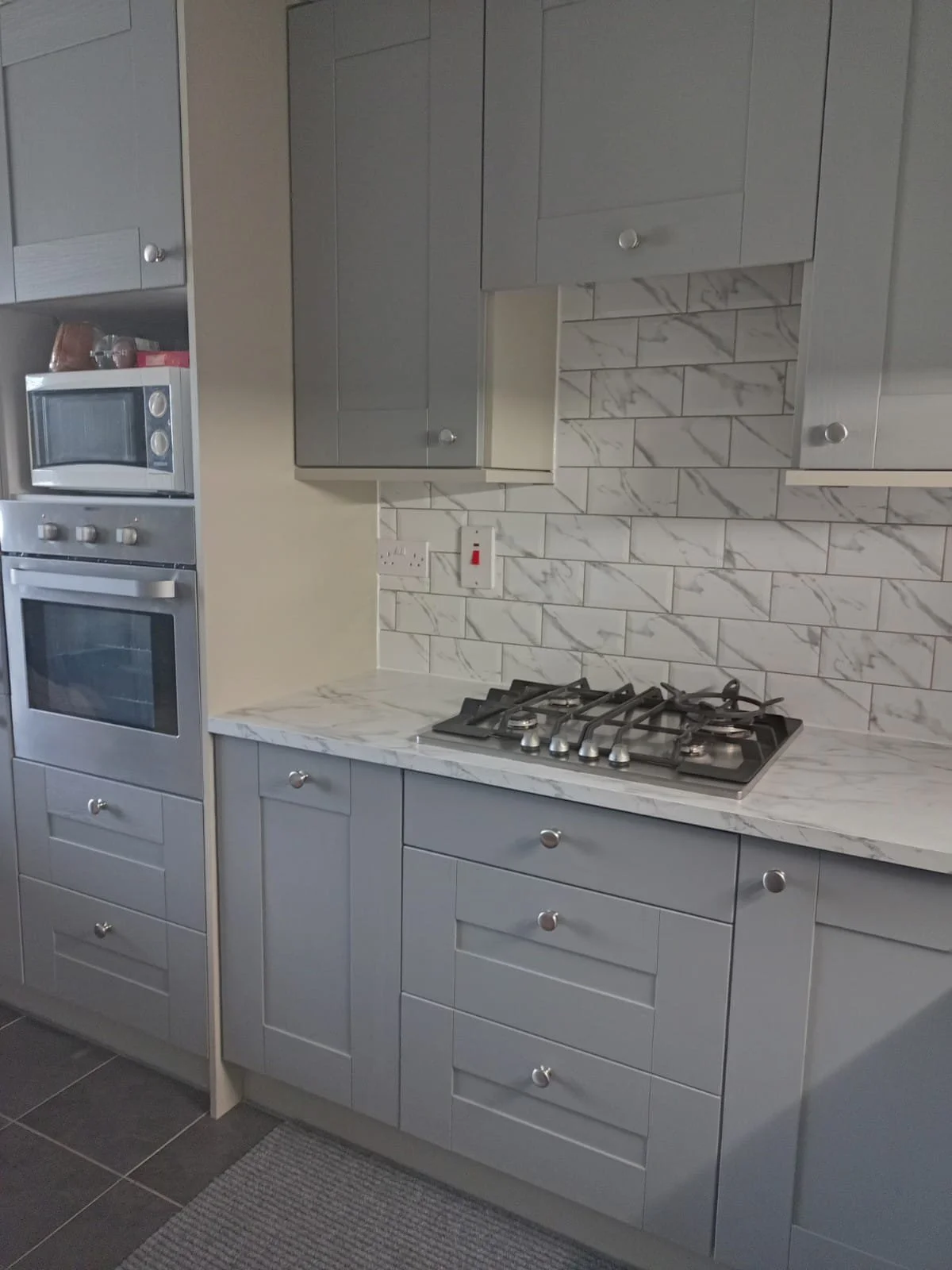 Kitchen with gray cabinets, marble countertop and backsplash, built-in oven and microwave, and a gas stove on the countertop.